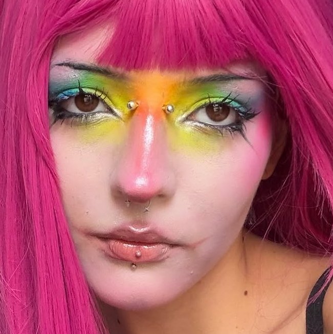 Close do rosto com maquiagem artística em arco-íris nos olhos, blush rosa e nariz rosado