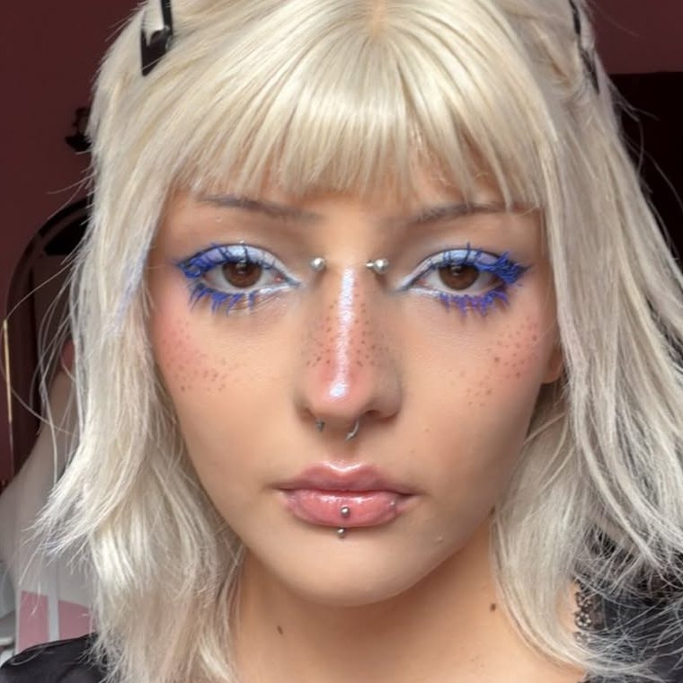 Close do rosto com delineado azul, sombra branca, sardas desenhadas e lábios com brilho